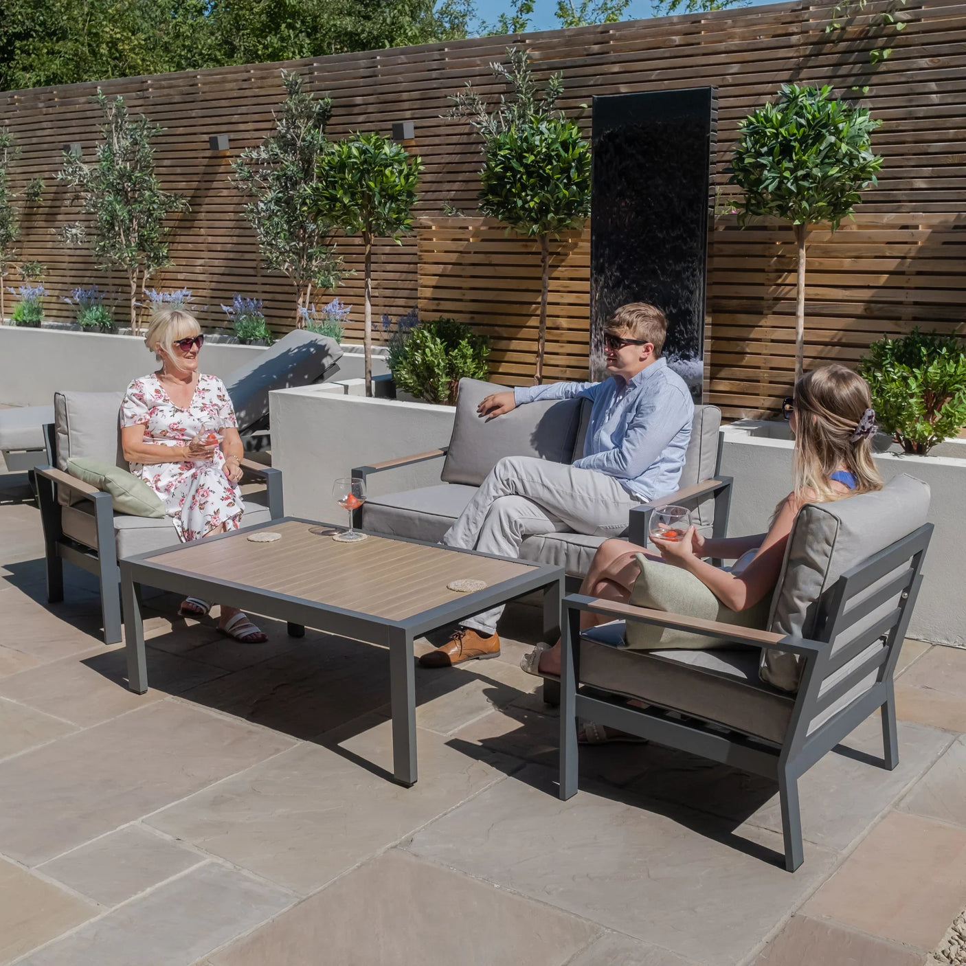 Grey metal outdoor sofa set with chairs and table on patio, people relaxing in garden seating