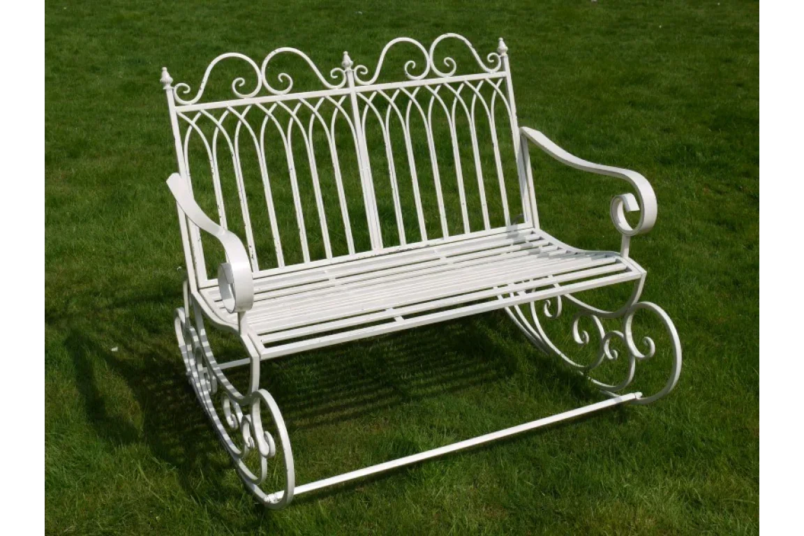White metal garden rocking bench with ornate scrollwork on grass