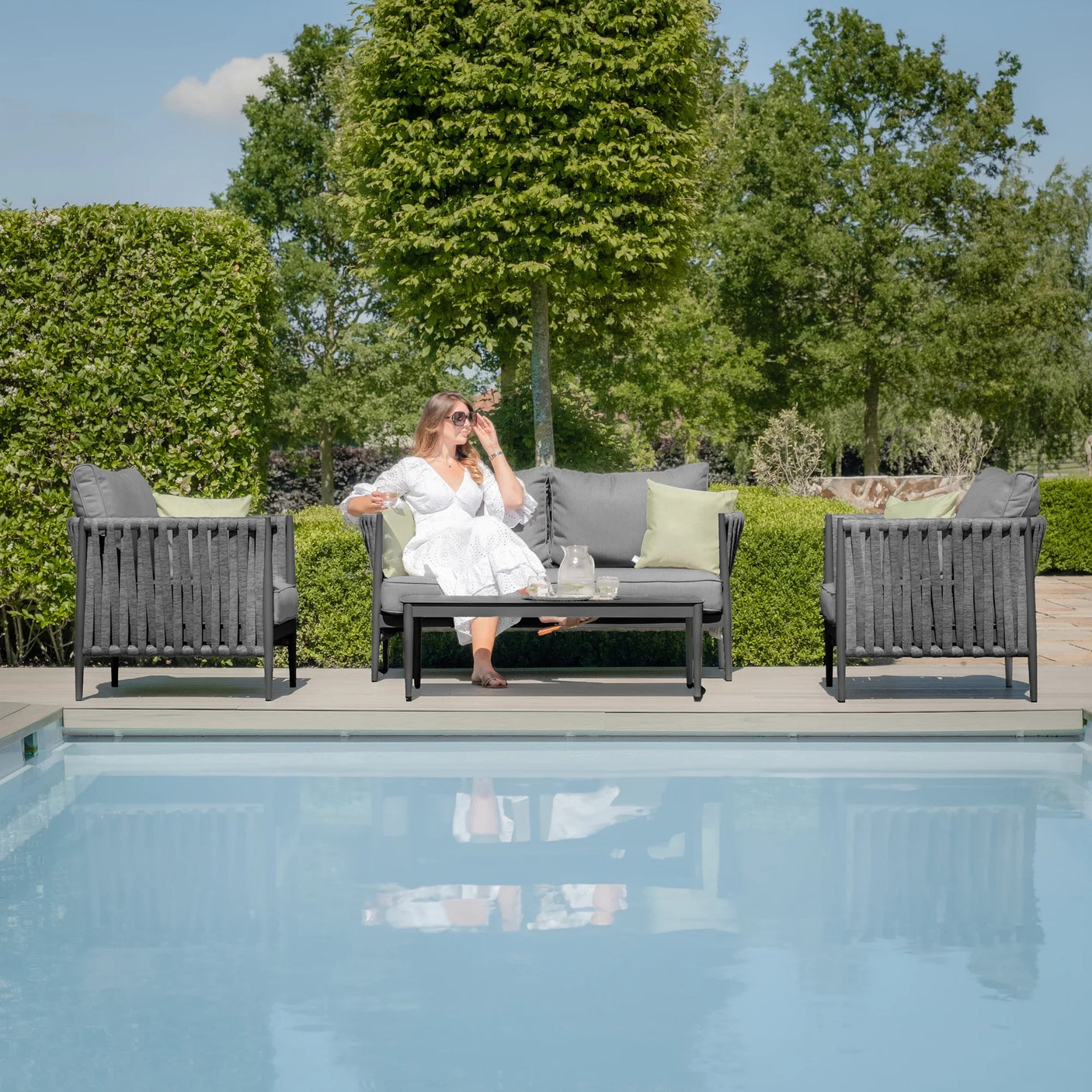 Grey outdoor garden sofa set with coffee table and armchairs beside a pool
