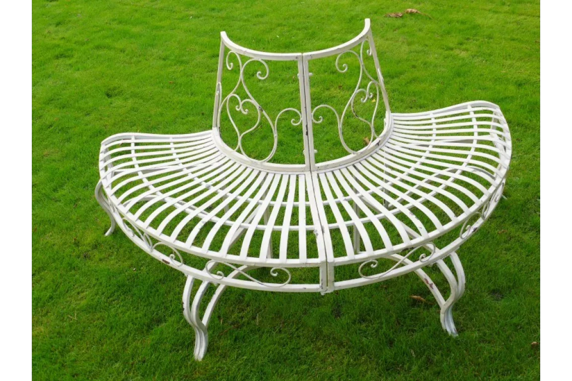 White metal tree bench with curved slatted seat and decorative scrollwork on green grass