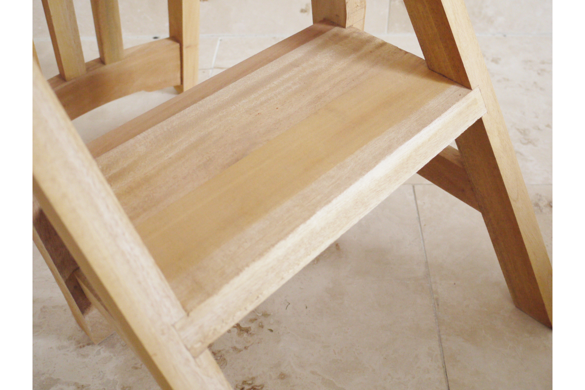 Unfinished light wood step stool viewed from angled side on tiled floor background.