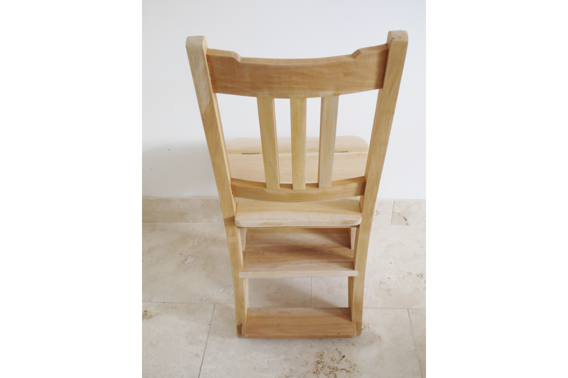 Unfinished wooden step chair with vertical slats, viewed from the back on a tiled floor against a white wall.