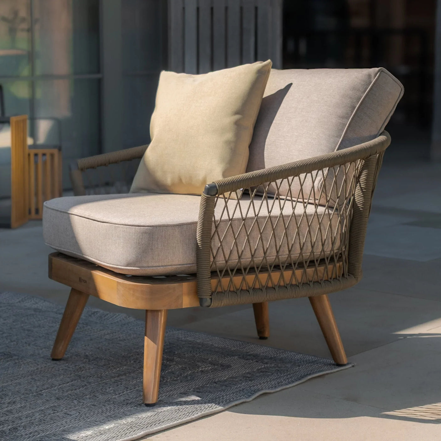 Outdoor armchair with light brown rope weave and beige cushions on patio rug