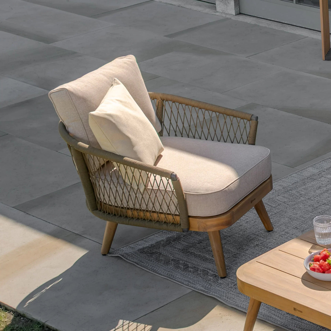 Beige outdoor armchair with woven rope sides and cushion on garden patio