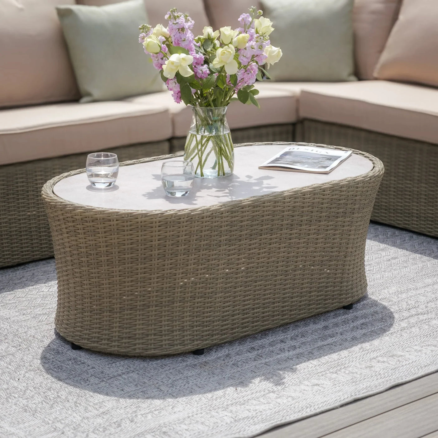 Rattan garden coffee table with glass top, vase of flowers and drinks, outdoor corner sofa