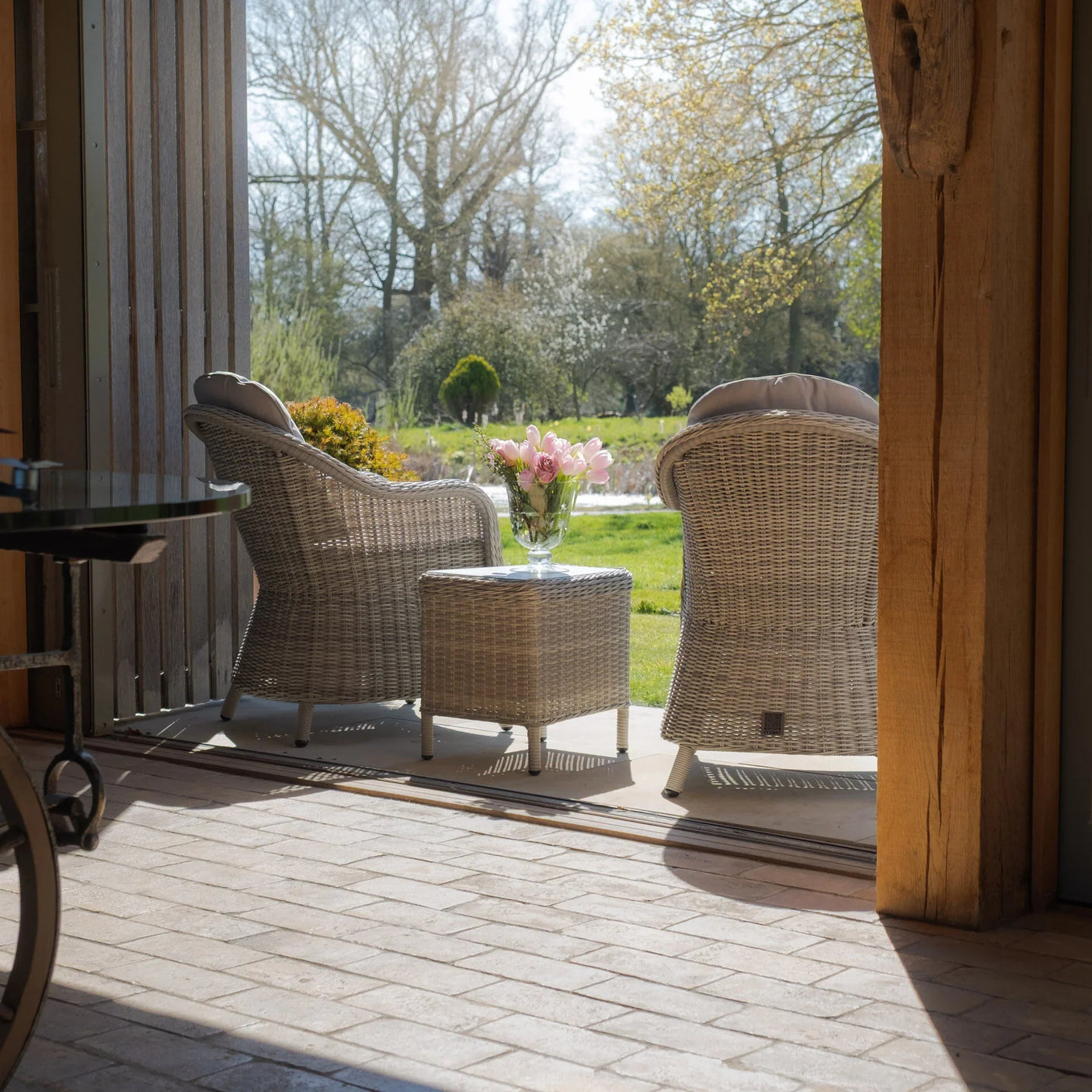 Rattan garden furniture set with two armchairs and table on patio, vase of pink flowers