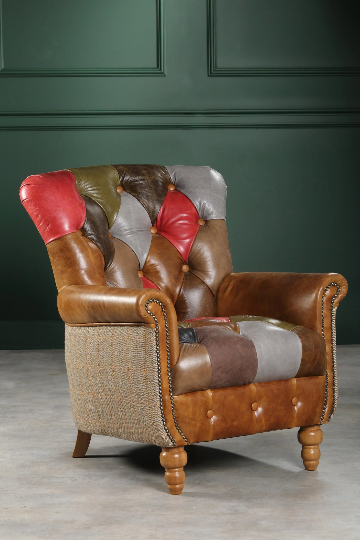 Patchwork leather armchair with studded detailing and turned wooden legs against dark green wall