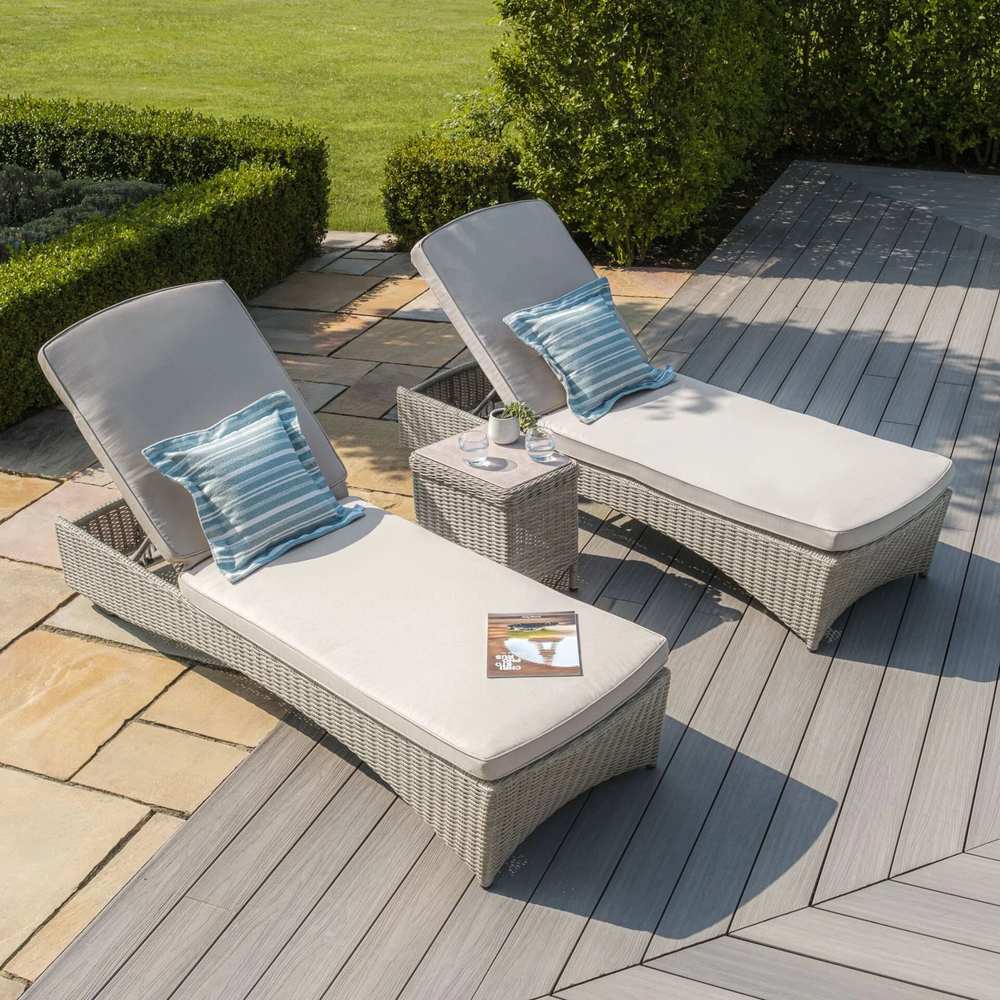 Rattan sun loungers with cream cushions and blue striped pillows on decking patio