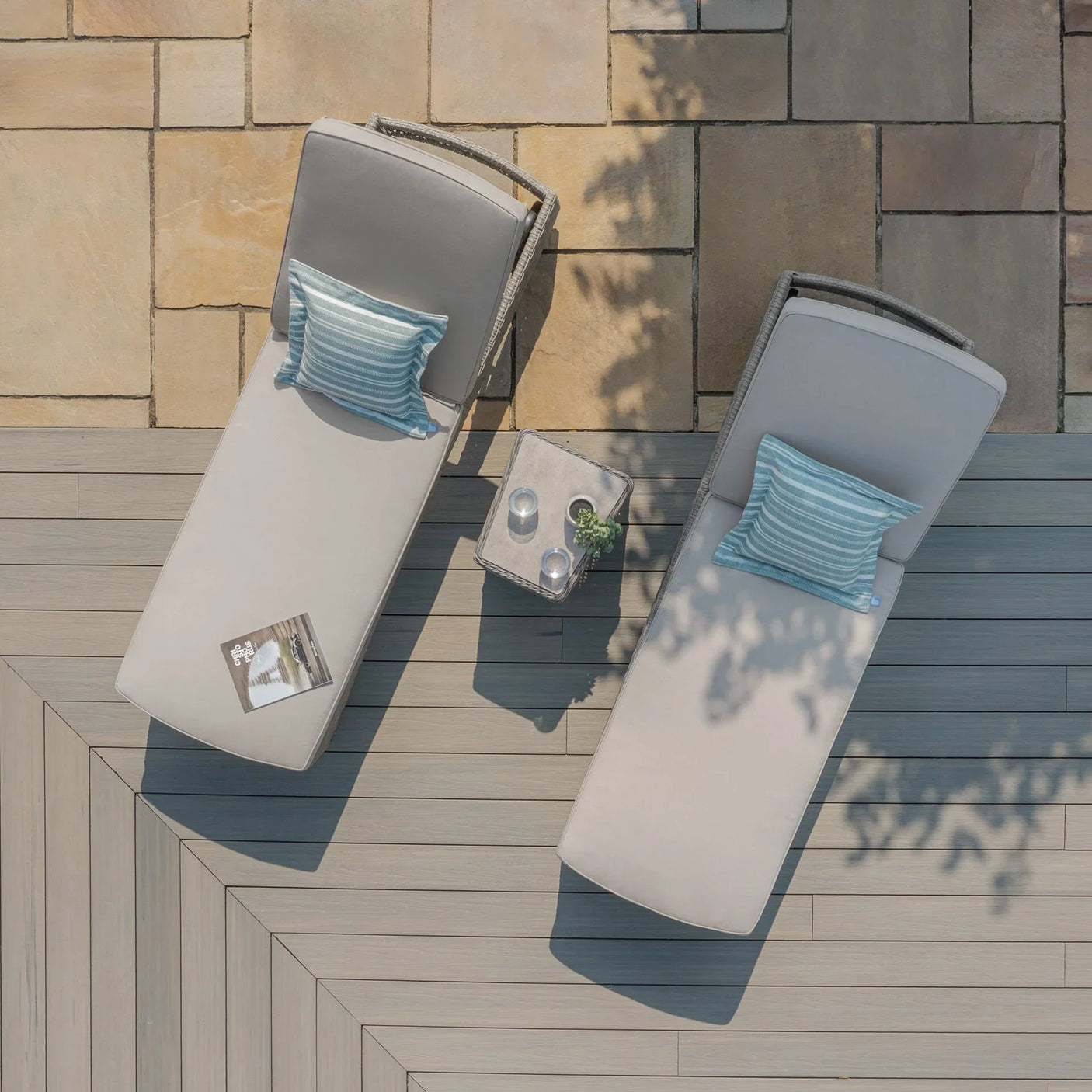 Rattan sun loungers with grey cushions and blue striped pillows on a patio decking