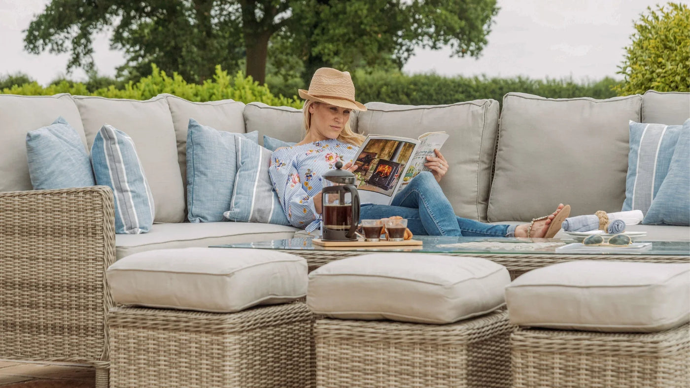 Rattan outdoor corner sofa set with beige cushions, blue pillows, and glass coffee table