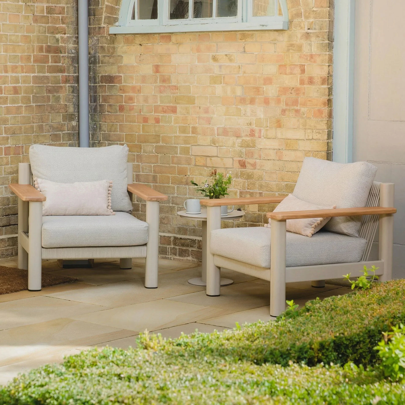 Beige garden armchairs with wooden armrests and cushions on patio next to side table