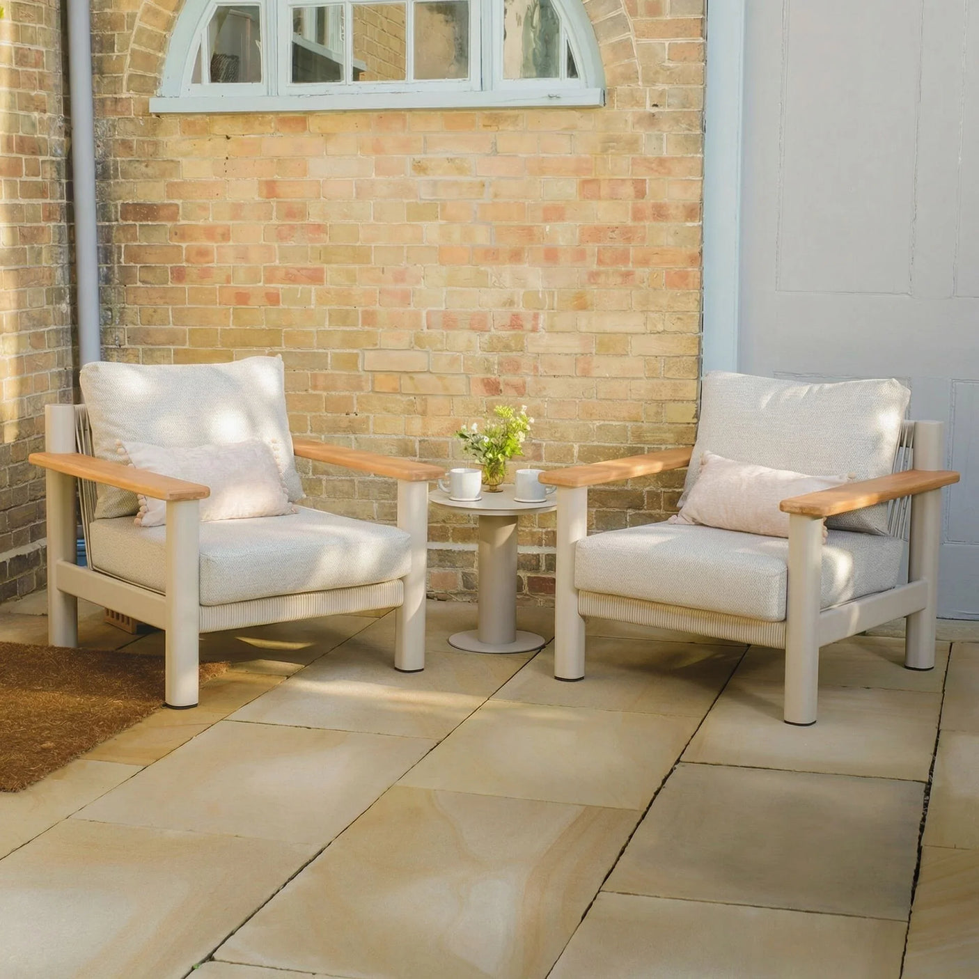 Outdoor garden armchair set with light cushions and wooden armrests on stone patio
