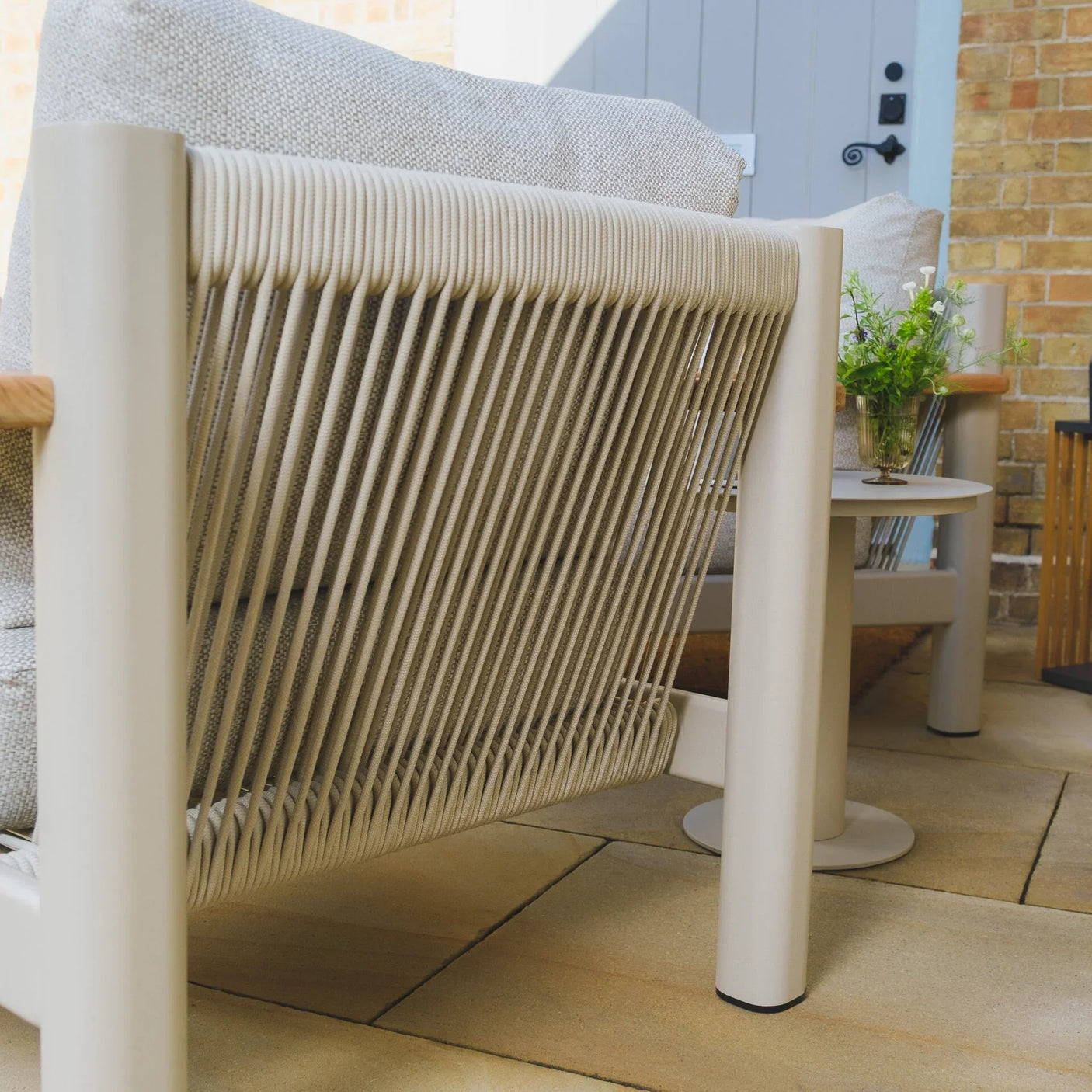 Beige rope outdoor sofa with textured cushions on a stone patio, close side angle