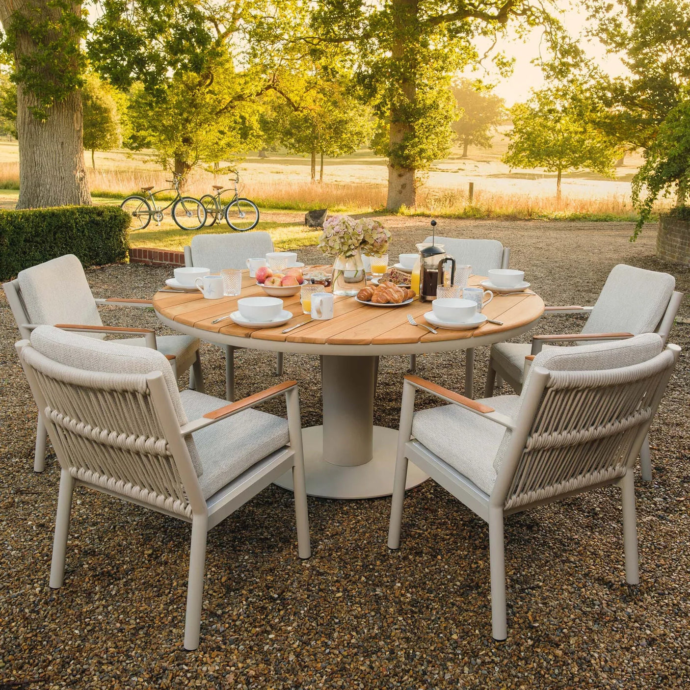 Round wooden outdoor dining table with six modern rope chairs set for breakfast on patio