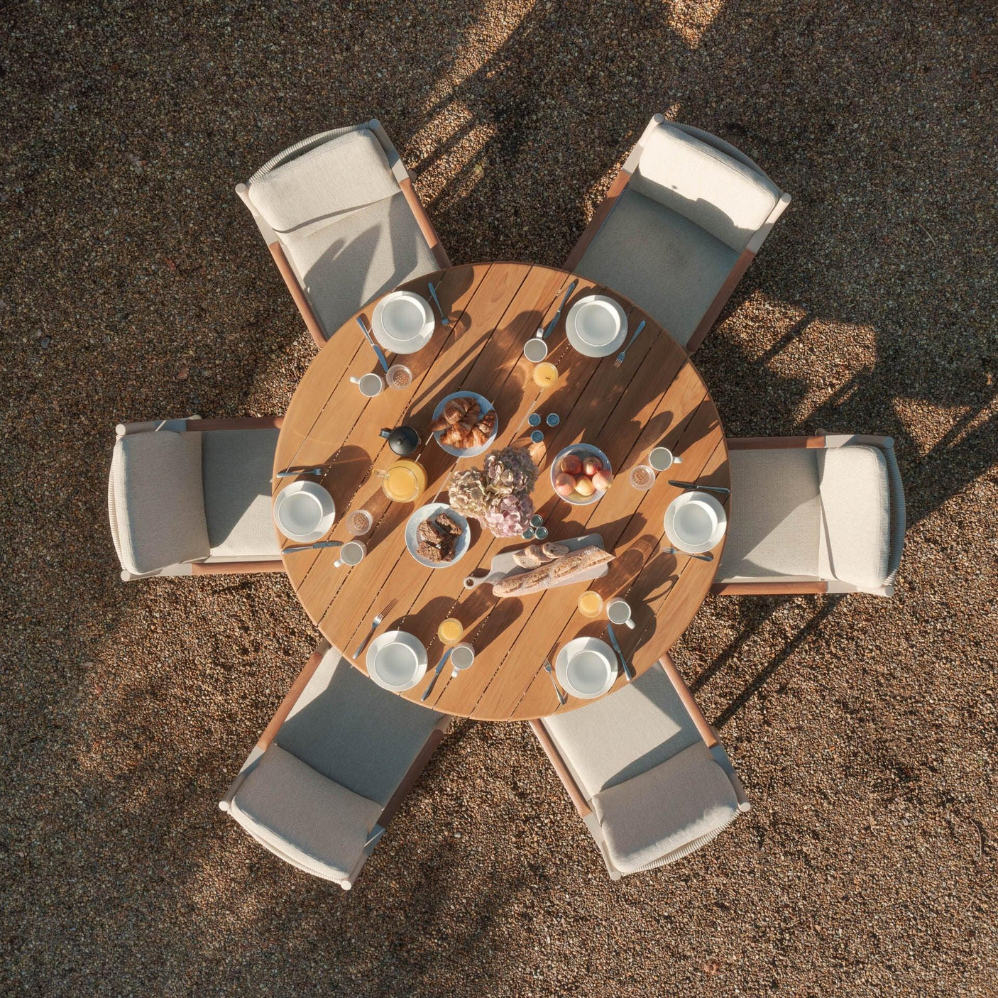 Round wooden garden dining table with six cushioned chairs set for outdoor breakfast