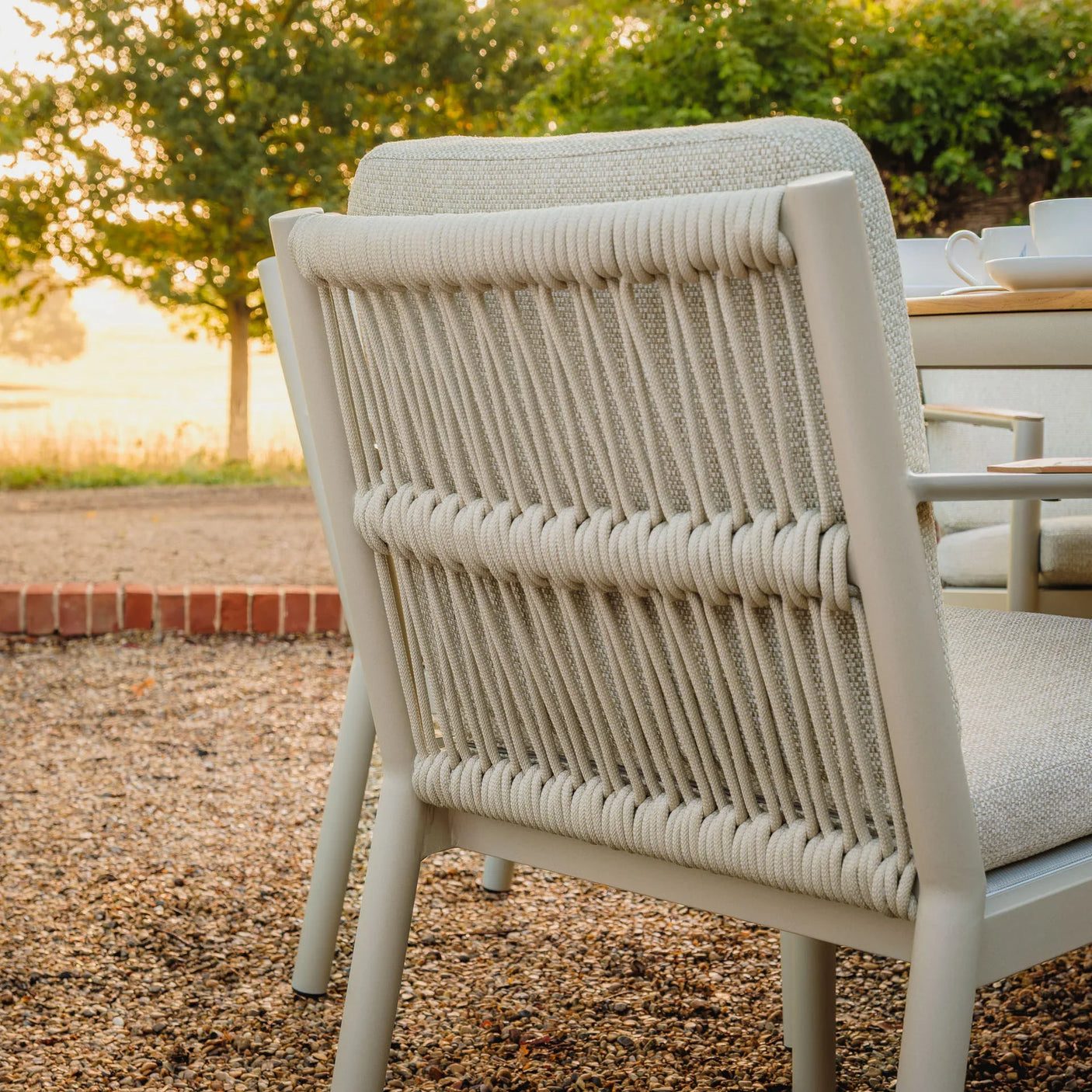 Beige rope weave outdoor dining chair with cushioned seat on gravel patio