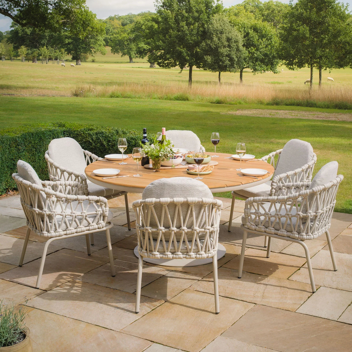 Outdoor garden dining set with round wooden table and six rope weave armchairs on patio