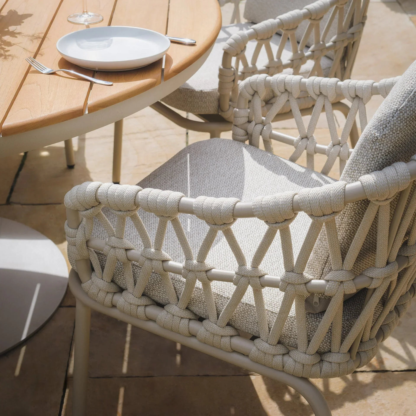 Outdoor rope weave dining chair with beige cushion beside slatted wooden patio table