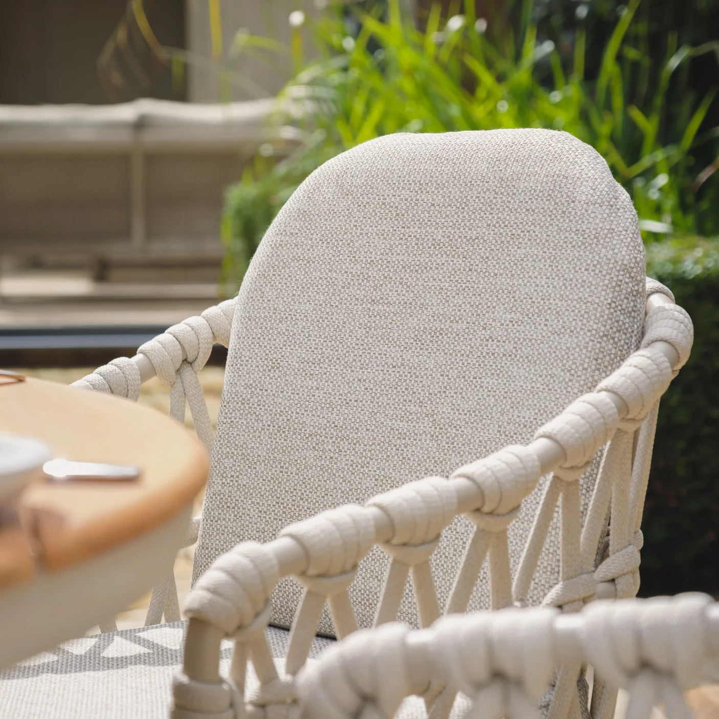 Beige woven outdoor dining chair with rope detail on armrests beside wooden table