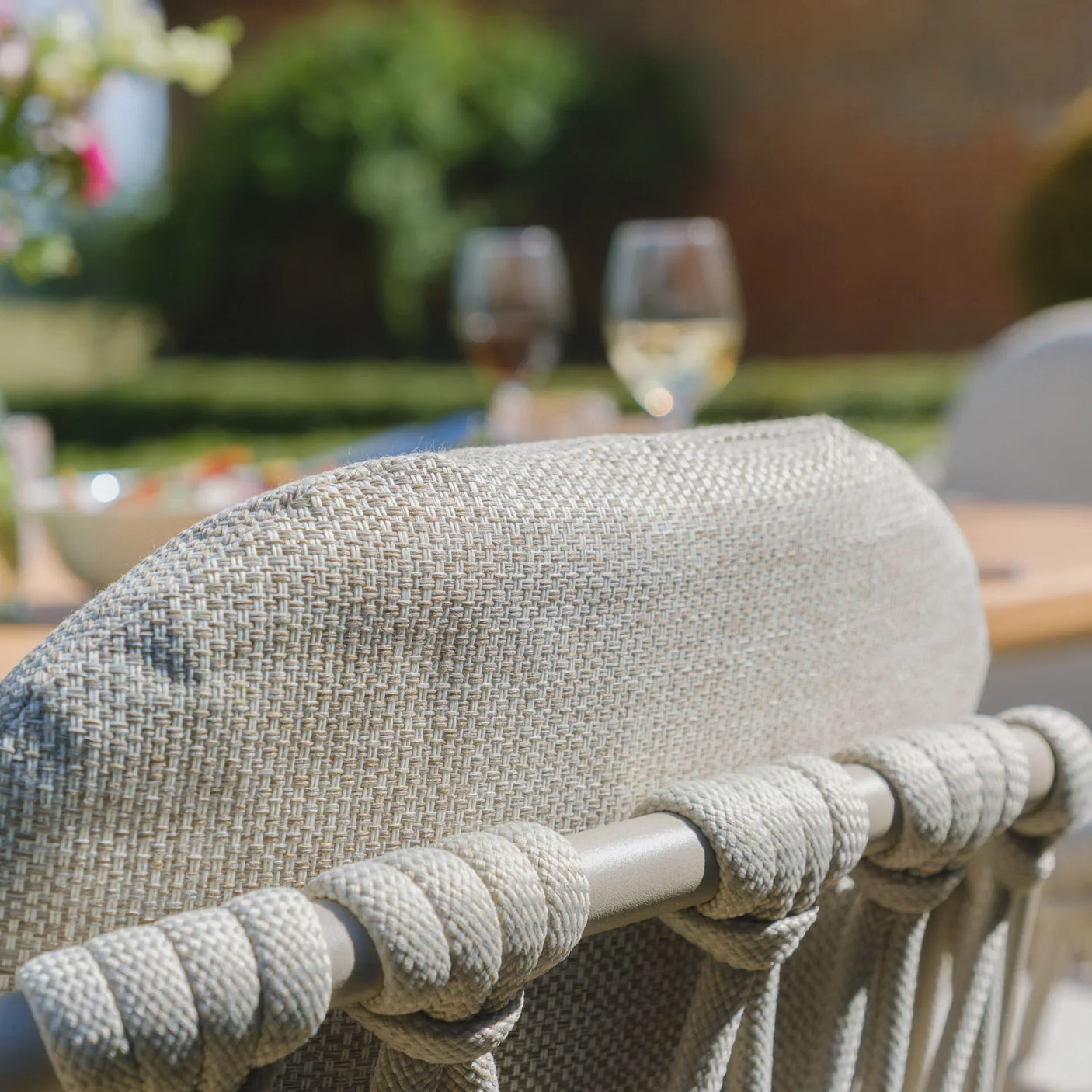 Woven rattan outdoor dining chair with rope detail, set at a garden table