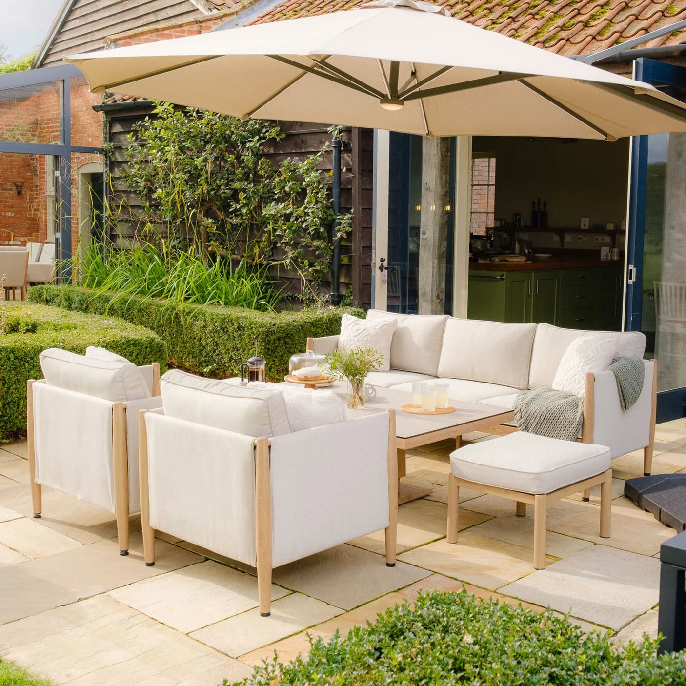 Beige outdoor garden furniture set with wooden frame and neutral cushions under large patio umbrella