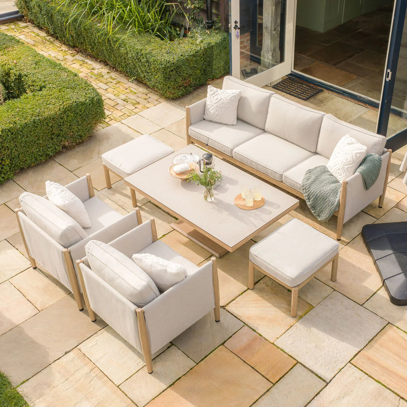 Beige outdoor garden sofa set with armchairs, footstool and table on stone patio