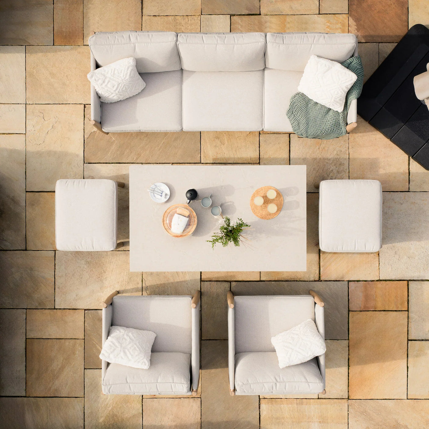 Beige outdoor sofa set with armchairs, footstools and dining table on stone patio