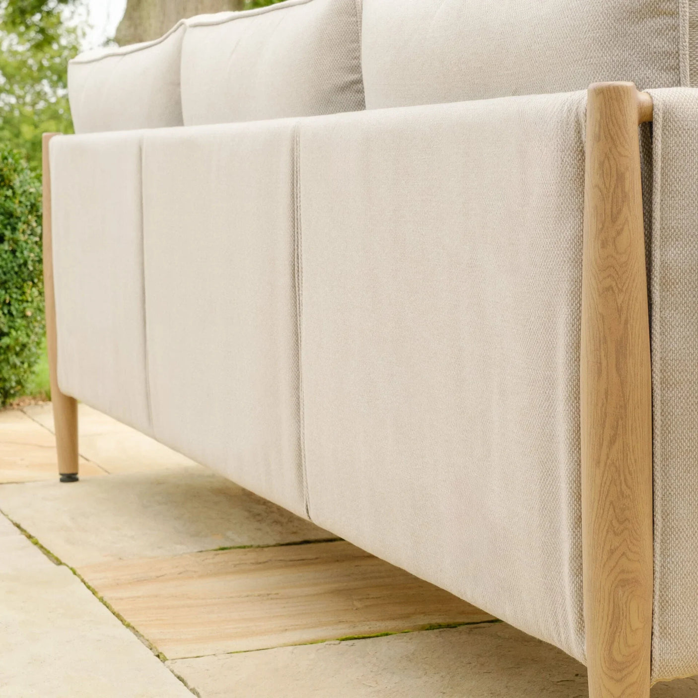 Beige outdoor sofa with light wood frame on stone patio