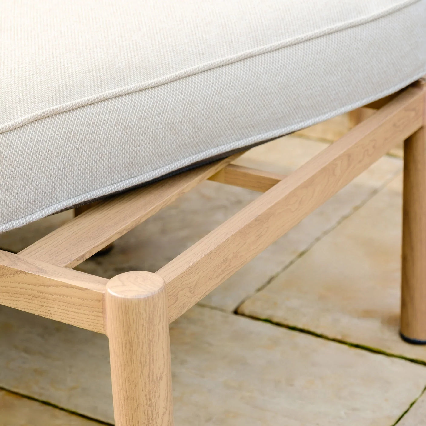Close-up of light wood sofa frame with cream fabric cushion on stone patio