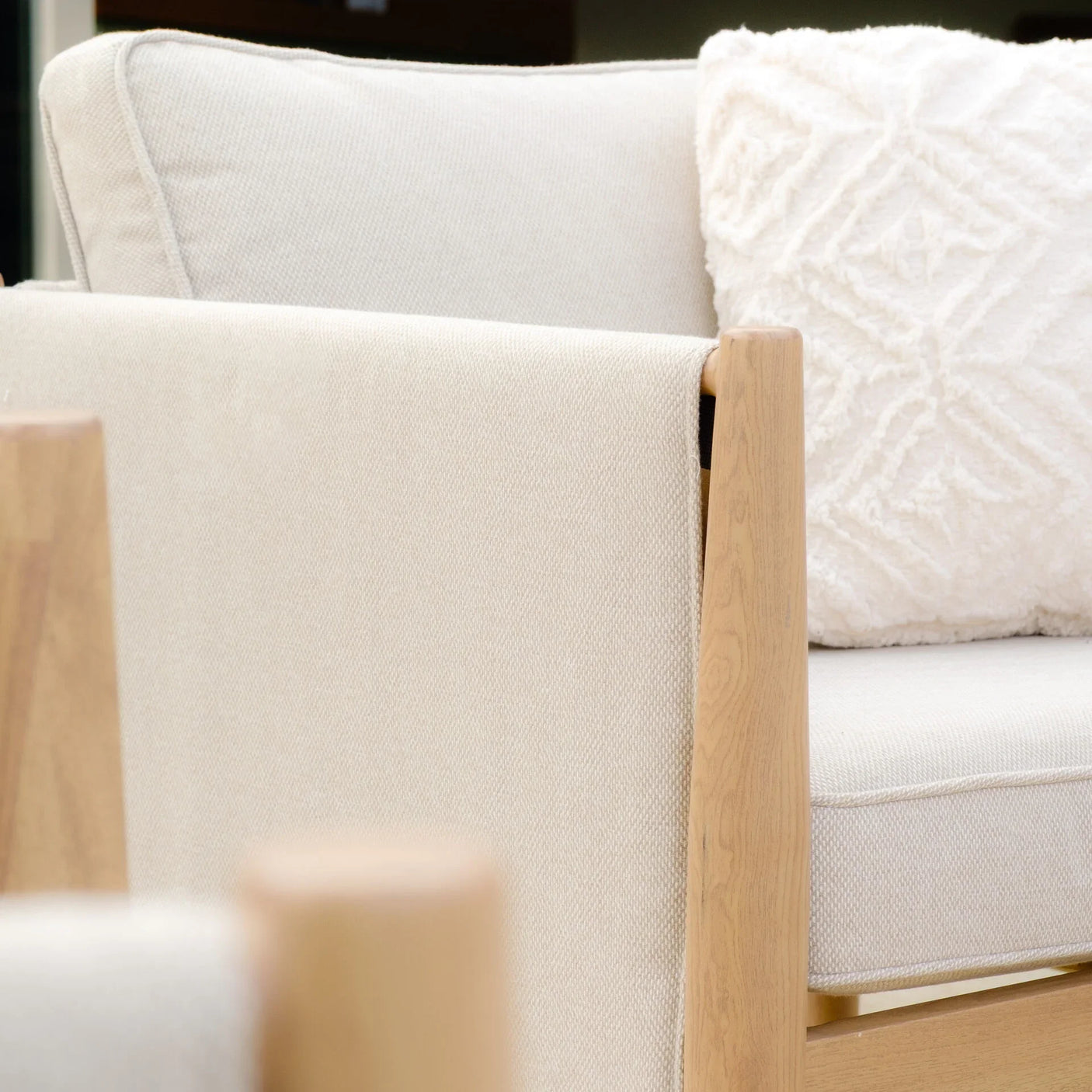 Beige fabric sofa with light wood armrest and textured cream cushion close-up