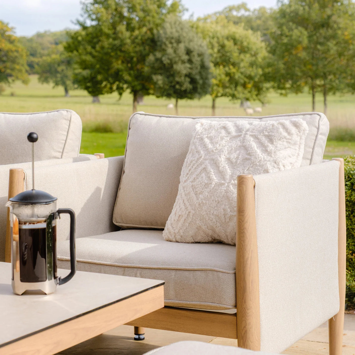 Beige outdoor armchair with wooden frame and textured cushion on patio next to coffee table