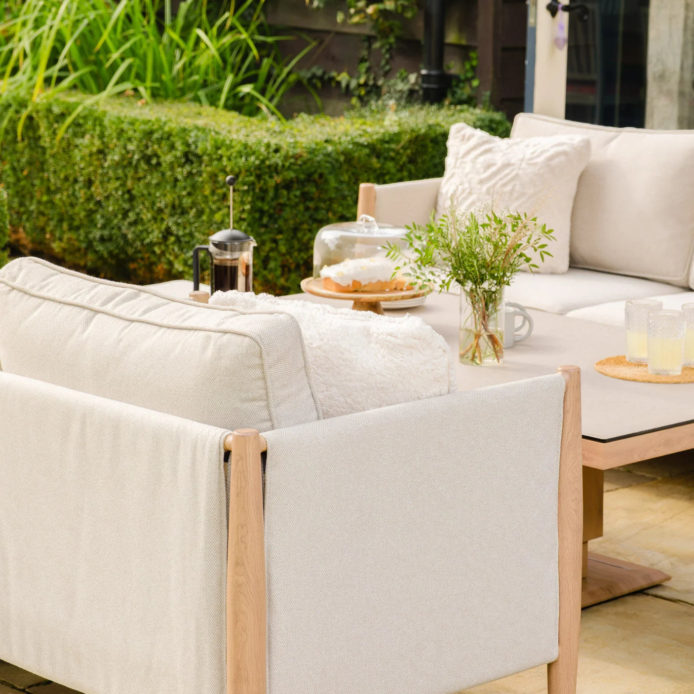 Cream outdoor corner sofa set with wooden frame and cushions beside garden table