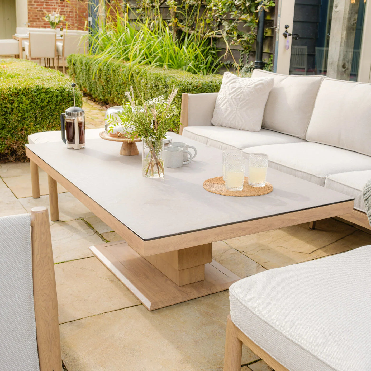 Outdoor wooden garden coffee table with drinks and flowers beside cream cushioned patio sofa
