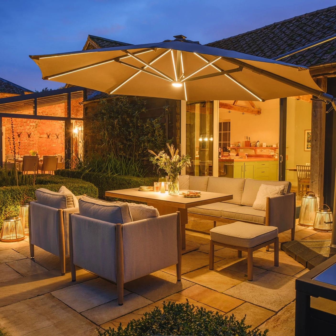 Outdoor patio furniture set with beige cushions under lighted garden parasol at dusk