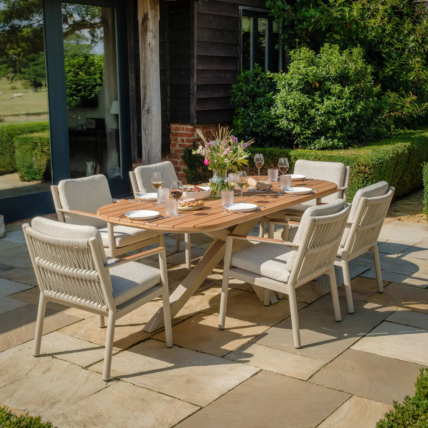 Outdoor dining set with wooden table and six cushioned garden chairs on stone patio