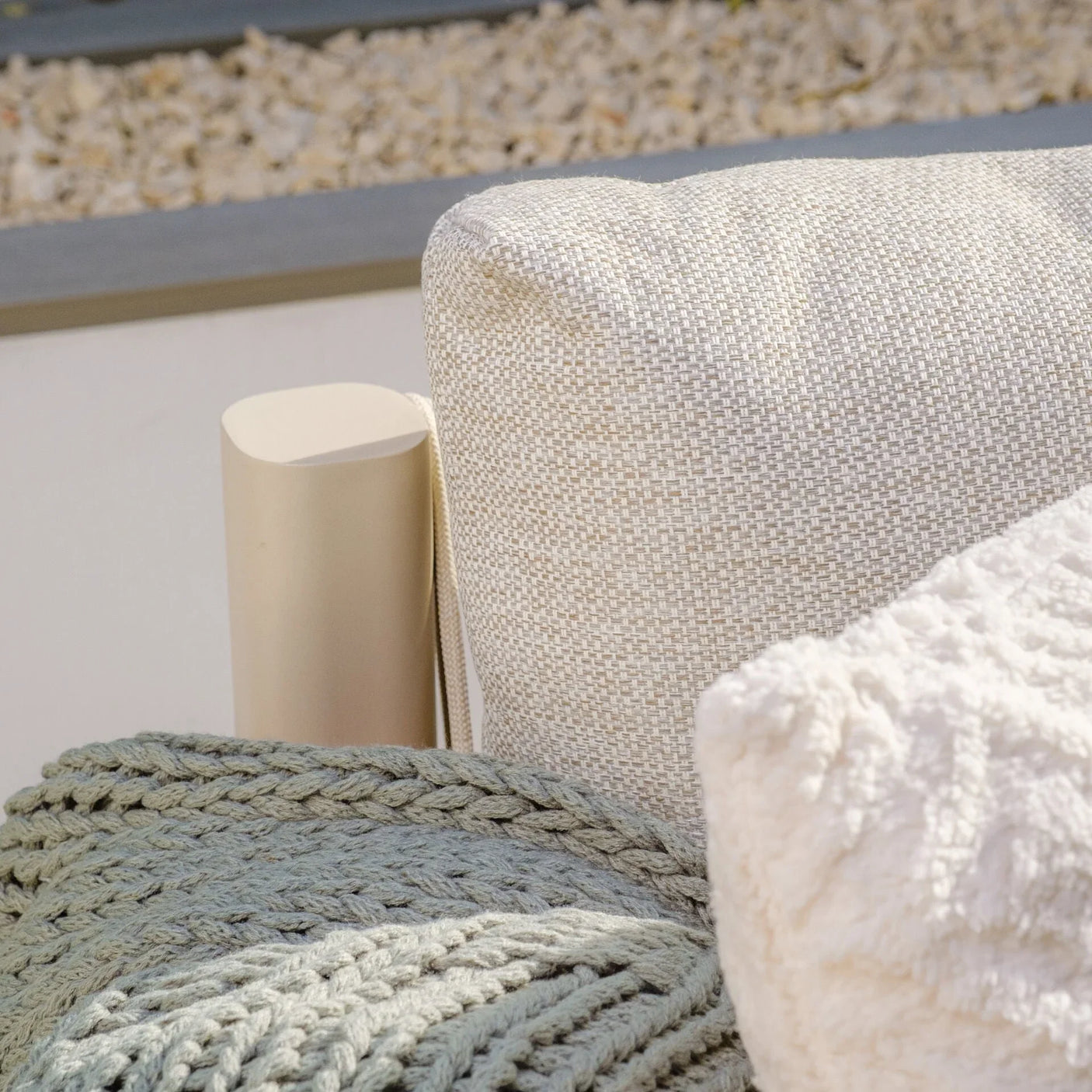 Closeup of outdoor sofa armrest with beige fabric cushion and textured throws