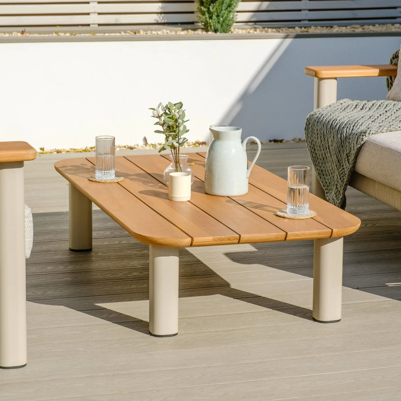 Outdoor coffee table with wood top and beige legs set on patio, glassware and decor placed on top