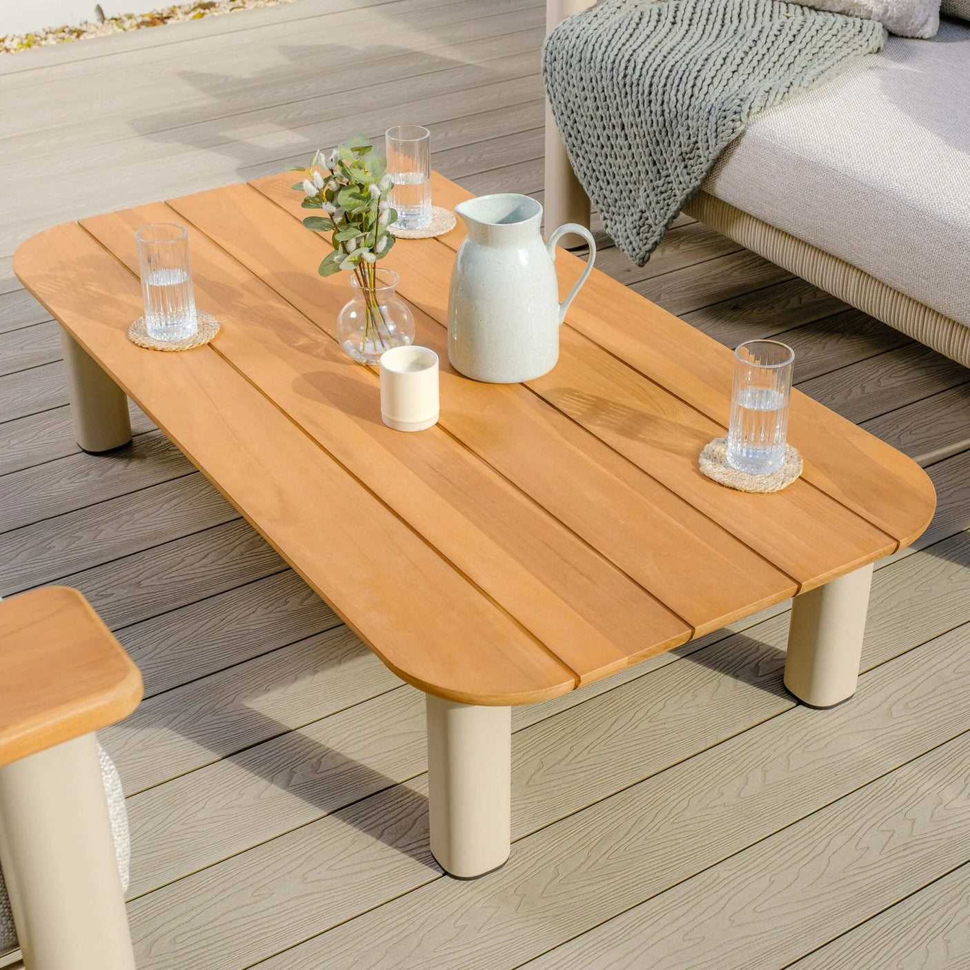 Wooden outdoor coffee table on decking with glasses, a jug, and decor items