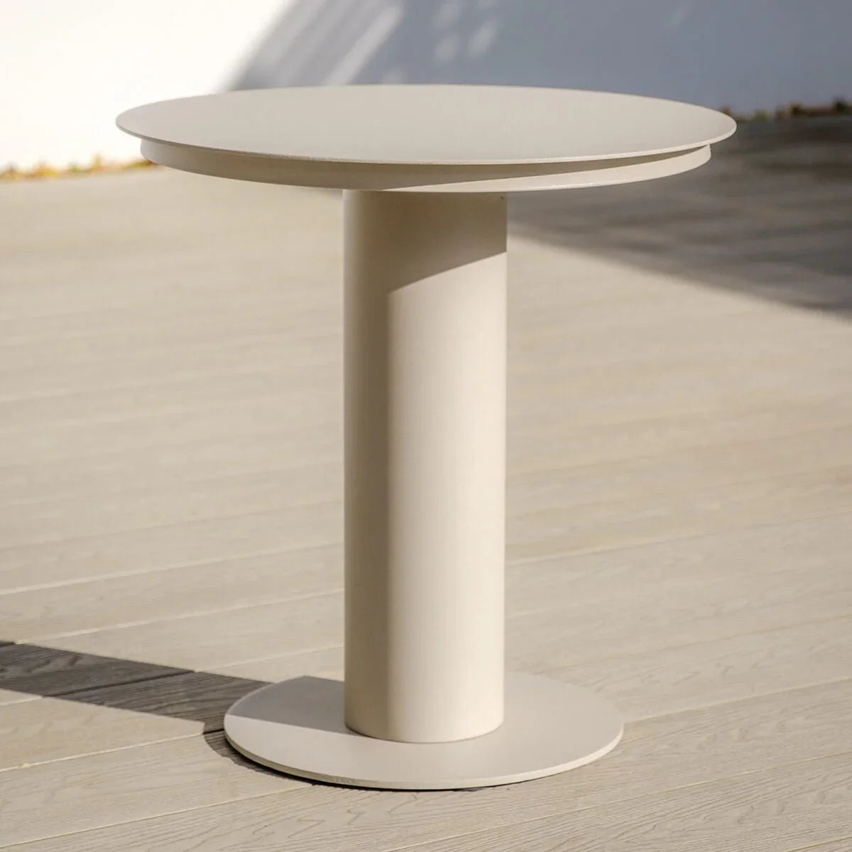 Round beige side table with pedestal base on wooden decking in sunlight