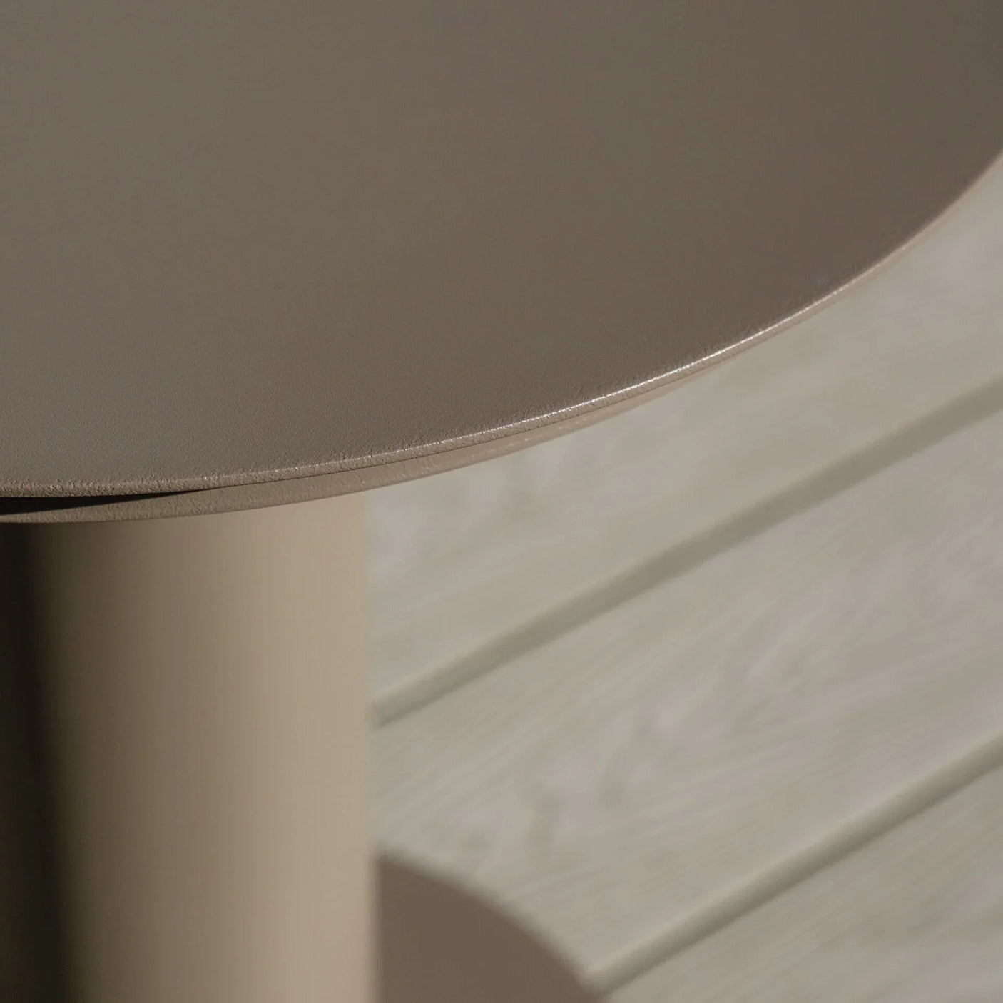 Round taupe metal side table with smooth finish on light wood decking