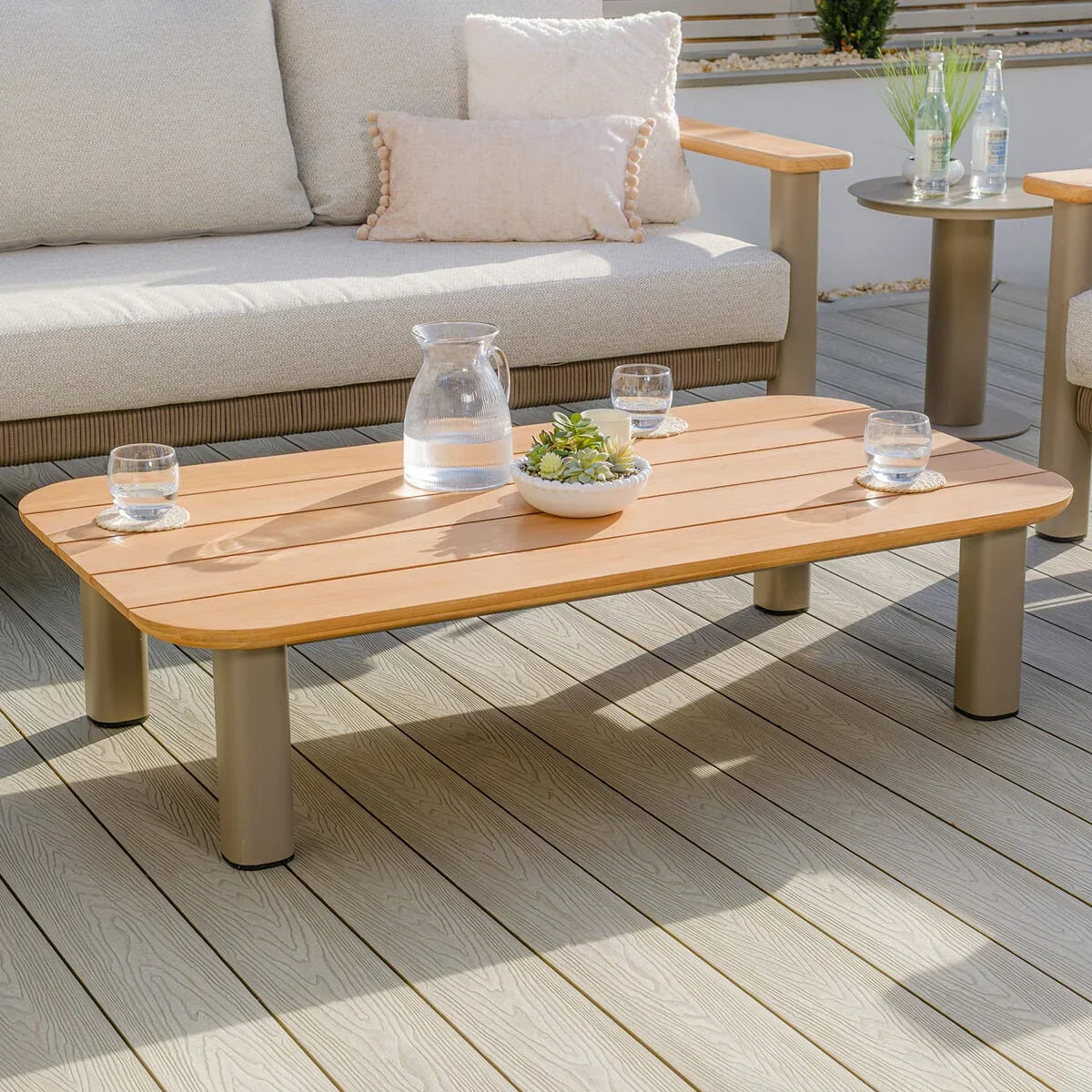 Rectangular wooden outdoor coffee table with metal legs on decking, set with glasses and jug