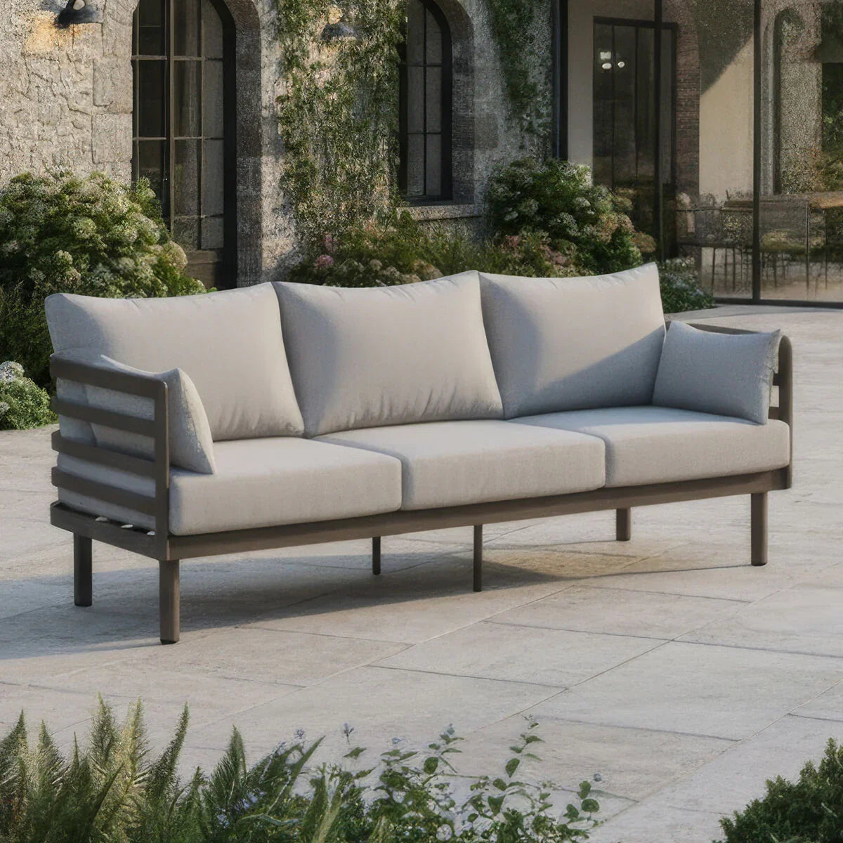 Outdoor patio sofa with light grey cushions and dark metal frame on stone flooring