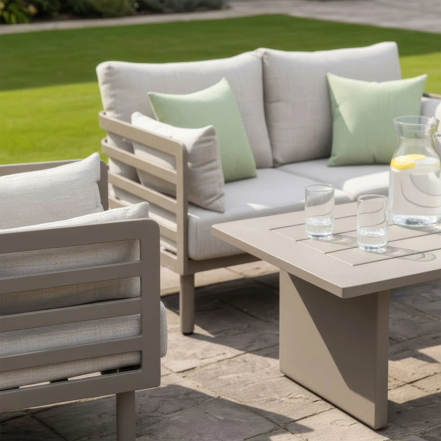 Beige outdoor sofa set with matching armchair, square table and green cushions on patio