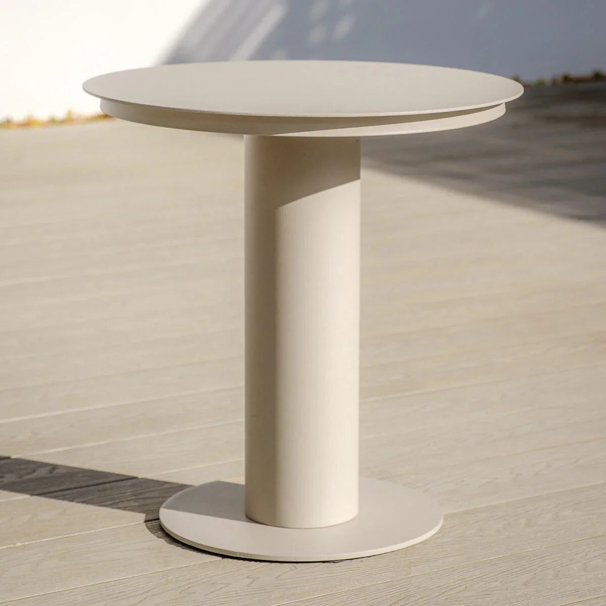 Round beige outdoor side table with pedestal base on light wood decking