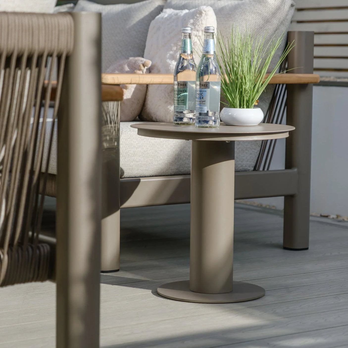 Taupe outdoor side table with drinks and plant beside rope armrest garden sofa