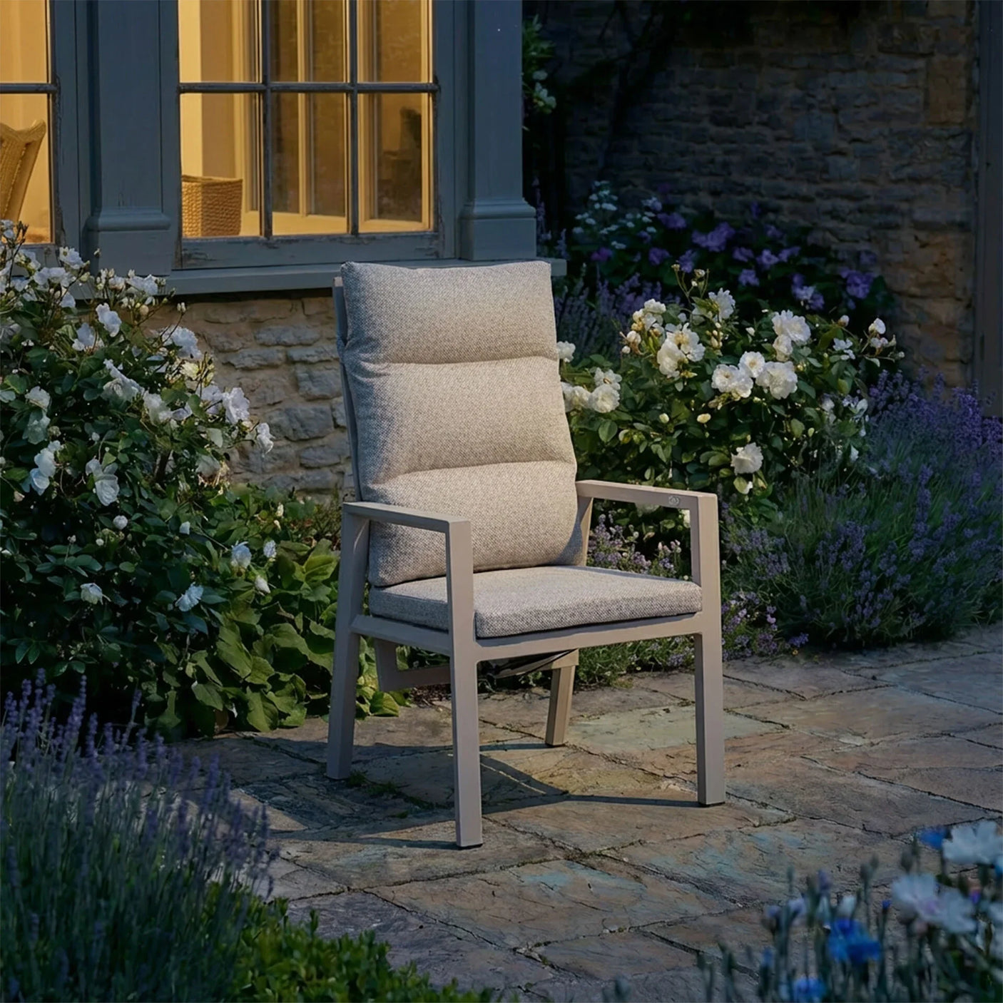 Beige outdoor garden chair with padded cushion on stone patio near blooming flowers