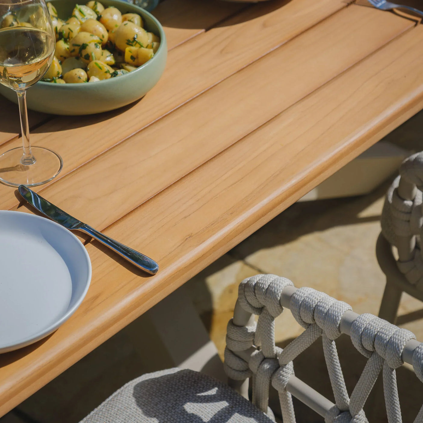 Wooden outdoor dining table with grey rope dining chair and plated food setting