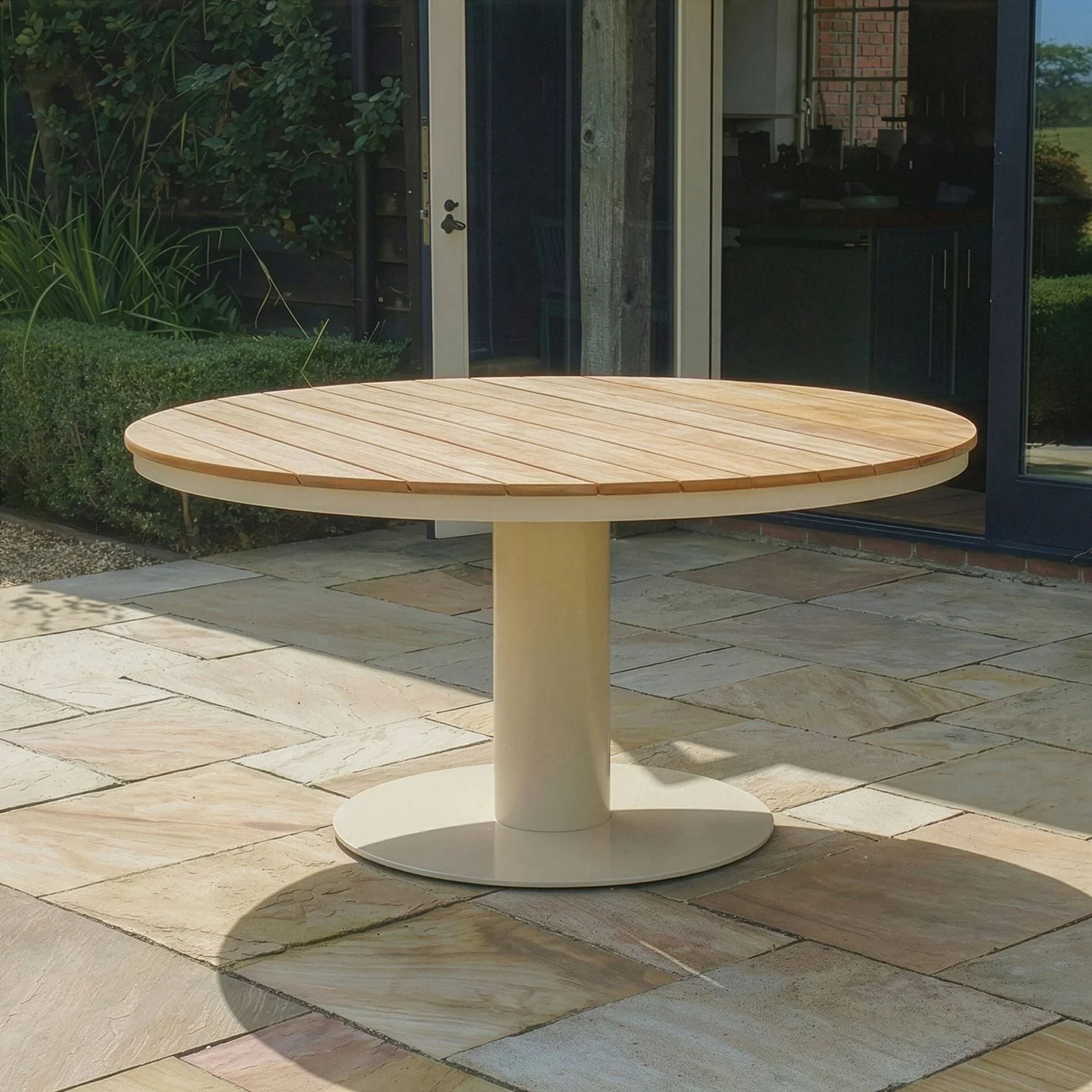 Round wooden outdoor dining table with cream pedestal base on patio