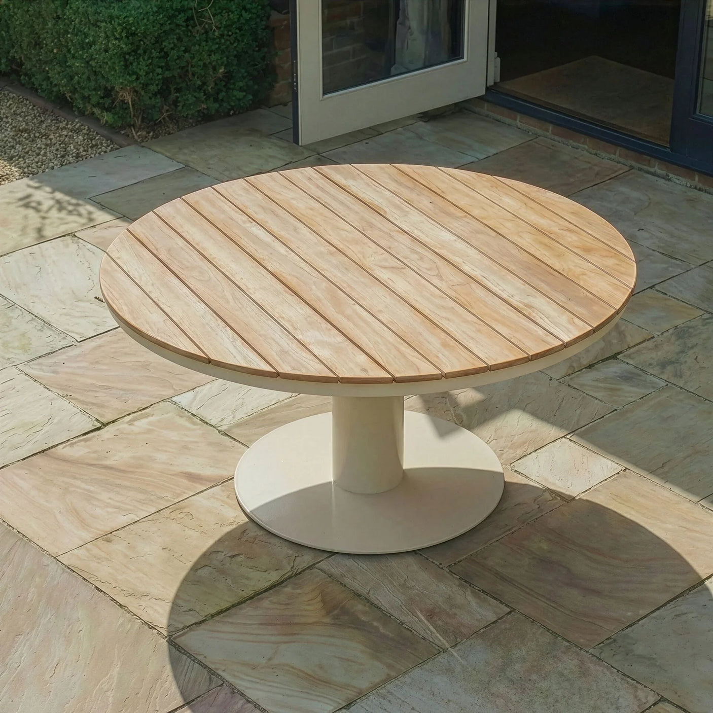 Round wooden outdoor dining table with slatted top and pedestal base on stone patio