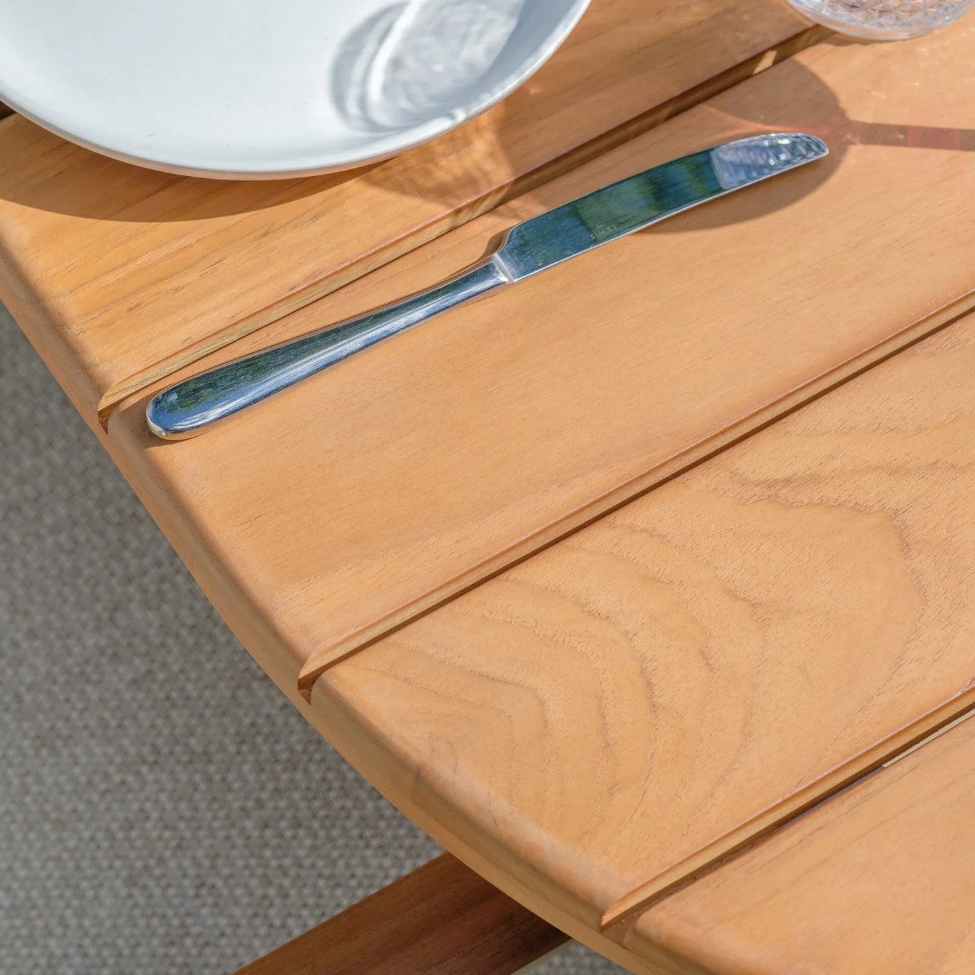 Close up of wooden outdoor dining table with plate, glassware, and metal knife